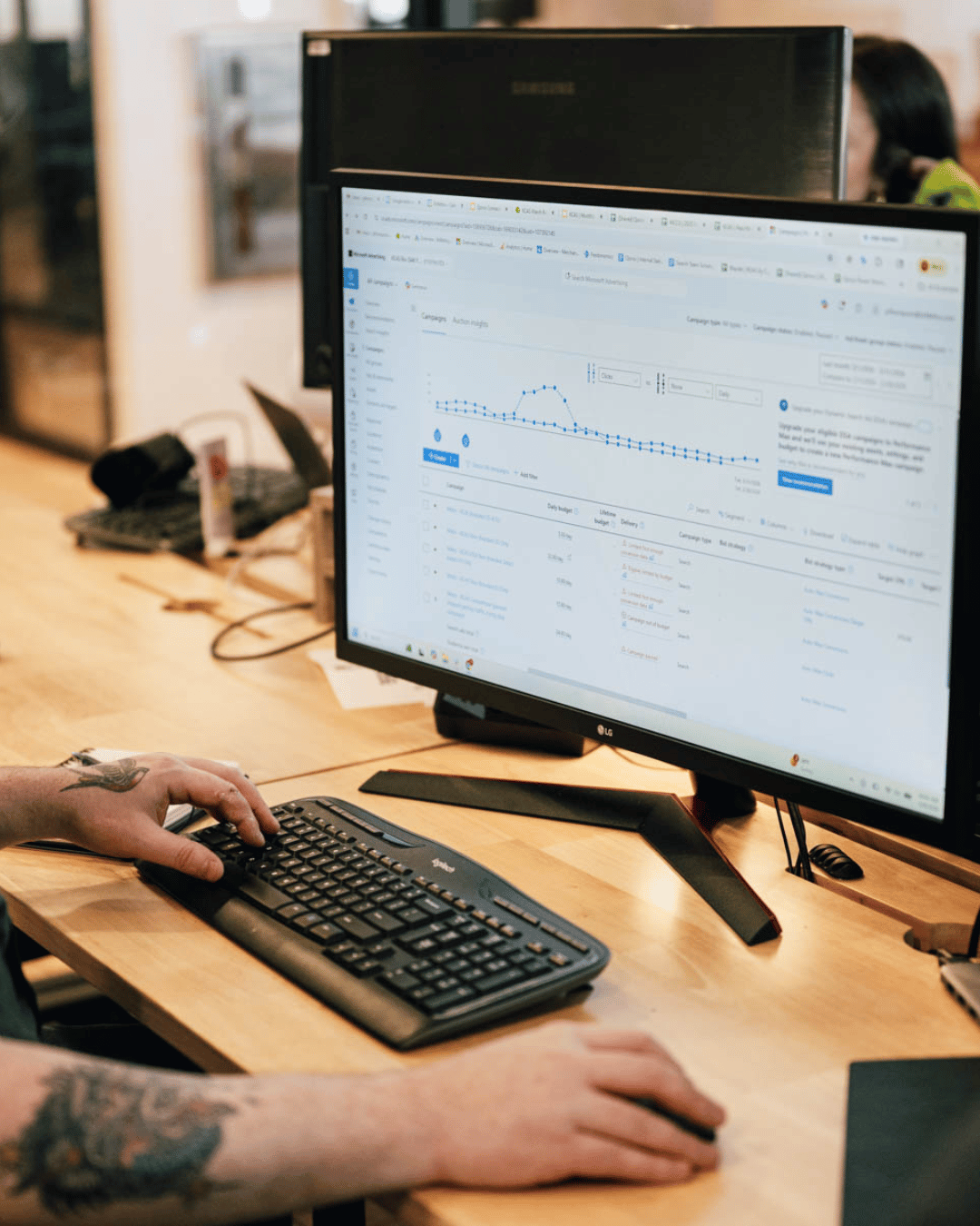 man with tattoos uses mouse to look at Google ads on desktop screen