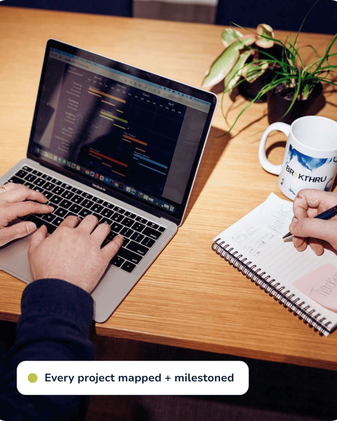 men typing and writing, looking at laptop screen that displays a gantt chart