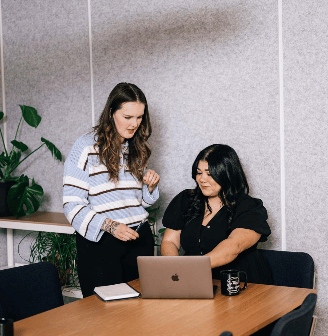 women collaborate at a table over laptop